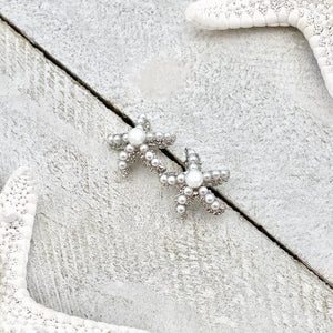 Dainty Pearl Starfish Stud Earrings are displayed on a white wooden surface.