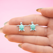 Load image into Gallery viewer, Enamel Sea Turtle Studs showcased between fingers for a close-up view.