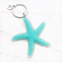 Load image into Gallery viewer, Happy Starfish Keychain displayed on a white wooden surface.