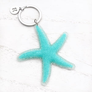 Happy Starfish Keychain displayed on a white wooden surface.
