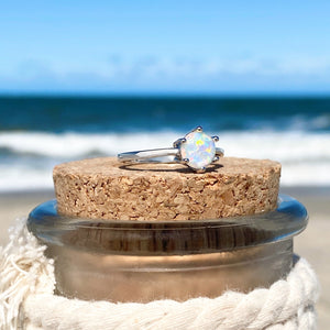 Minimalist Opal Ring displayed by being placed on top of a cork with a blurred beach background.