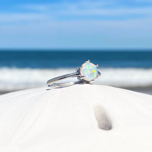 Minimalist Opal Ring displayed by being placed on top of white dome with a blurred beach background.