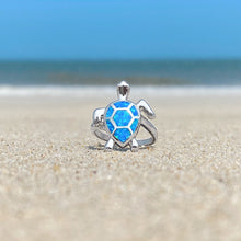 Load image into Gallery viewer, Opal Swimming Sea Turtle Ring is showcased on the sandy shore against a blurred beach background.