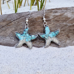 Sand Starfish Earrings in Teal Turquoise are displayed by being placed on top of a driftwood on the sand.