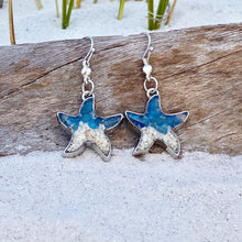 Load image into Gallery viewer, Sand Starfish Earrings in Blue Glass are displayed by being placed on top of a driftwood on the sand.