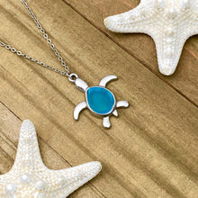 Load image into Gallery viewer, Sea Glass Sea Turtle Necklace in Sky Blue is displayed on a wooden surface.