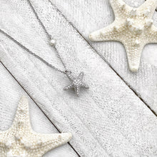 Load image into Gallery viewer, Starfish Hidden Pearl Necklace displayed on a white wooden surface.