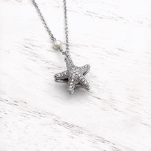 Load image into Gallery viewer, Starfish Hidden Pearl Necklace displayed on a white wooden surface.