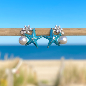 Starfish Pearl Studs displayed closely by being stuck to a wooden stick with a blurred beach background.