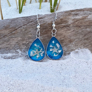 Under the Sea Earrings are displayed by being placed on top of a driftwood on the sand.