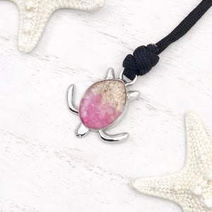 Black Rope Sand Sea Turtle Bracelet in Pink Pebble is displayed on a white wooden surface.