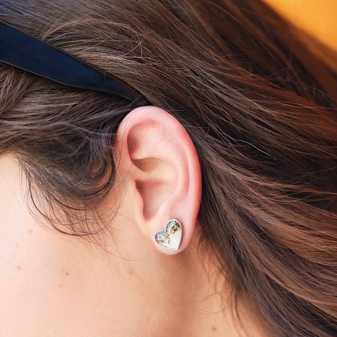 Abalone Sand Heart Studs is displayed up close by being worn on a woman's ear.