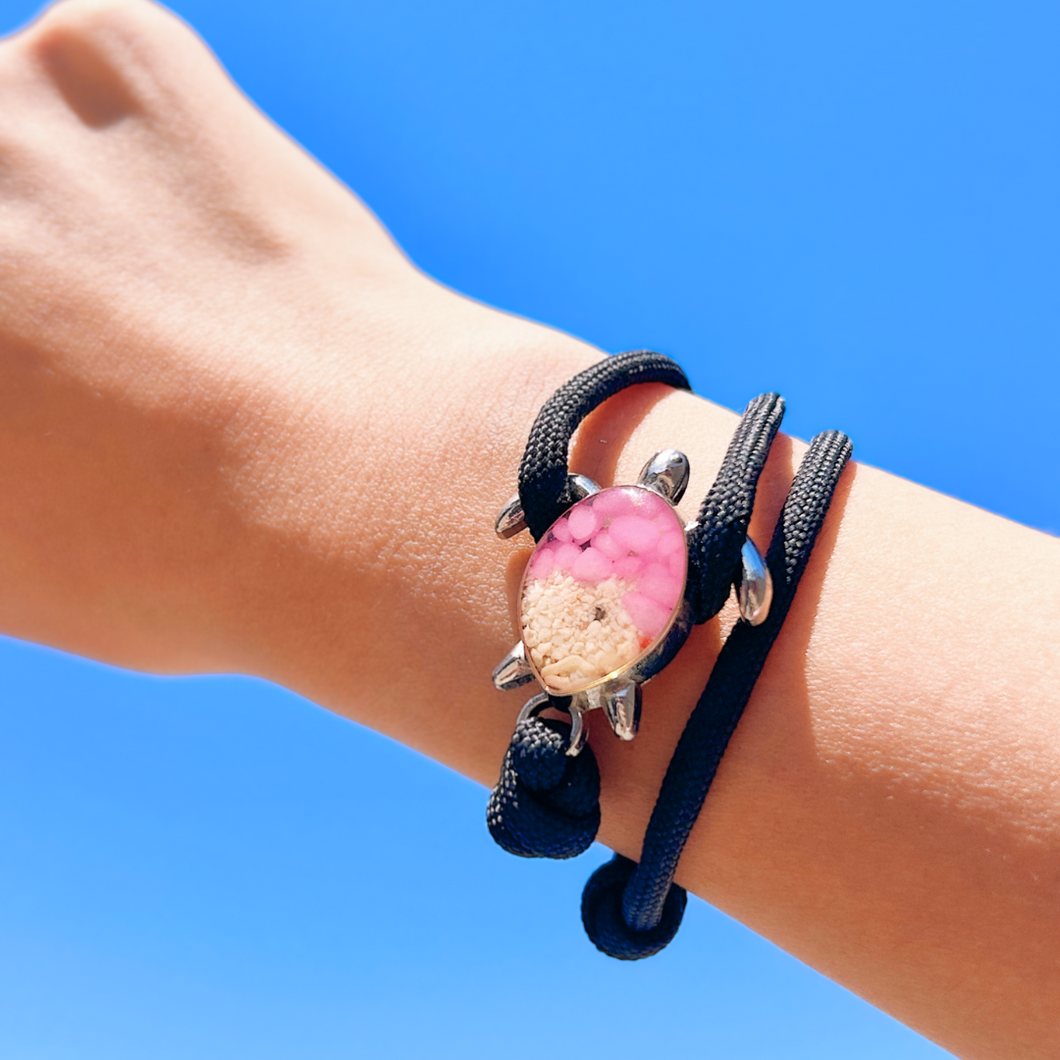Black Rope Sand Sea Turtle Bracelet with Pink Pebbles is displayed by being worn around a woman's wrist.