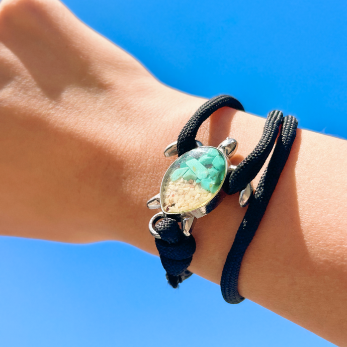 Black Rope Sand Sea Turtle Bracelet in Teal Turquoise is displayed by being worn around a woman's wrist.