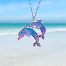 Load image into Gallery viewer, Colorful Enamel Dolphin Necklace hanging close for a shot with a blurred beach background.