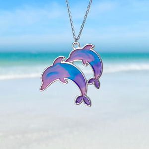 Colorful Enamel Dolphin Necklace hanging close for a shot with a blurred beach background.