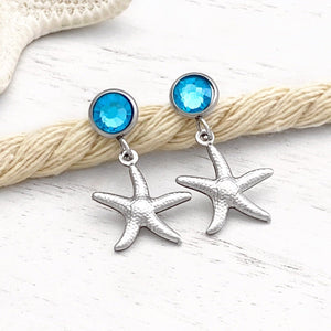Crystal Stud Starfish Earrings are placed on a thick rope on a white wooden surface.