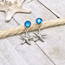 Load image into Gallery viewer, Crystal Stud Starfish Earrings are placed on a thick rope on a white wooden surface.