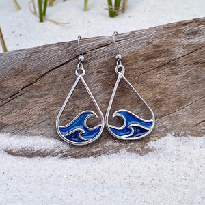 Curling Wave Earrings are displayed by being placed on top of a driftwood on the sand.