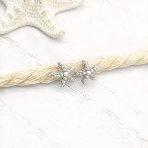 Dainty Pearl Starfish Stud Earrings displayed on a thick rope atop a white wooden surface.