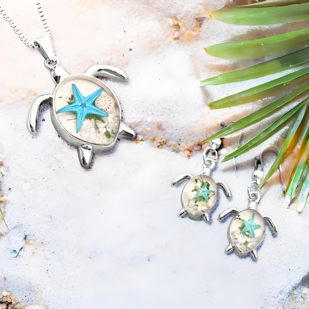 Deep in the Ocean Sea Turtle earrings and necklace showcased on a sandy surface with a palm leaf accent.
