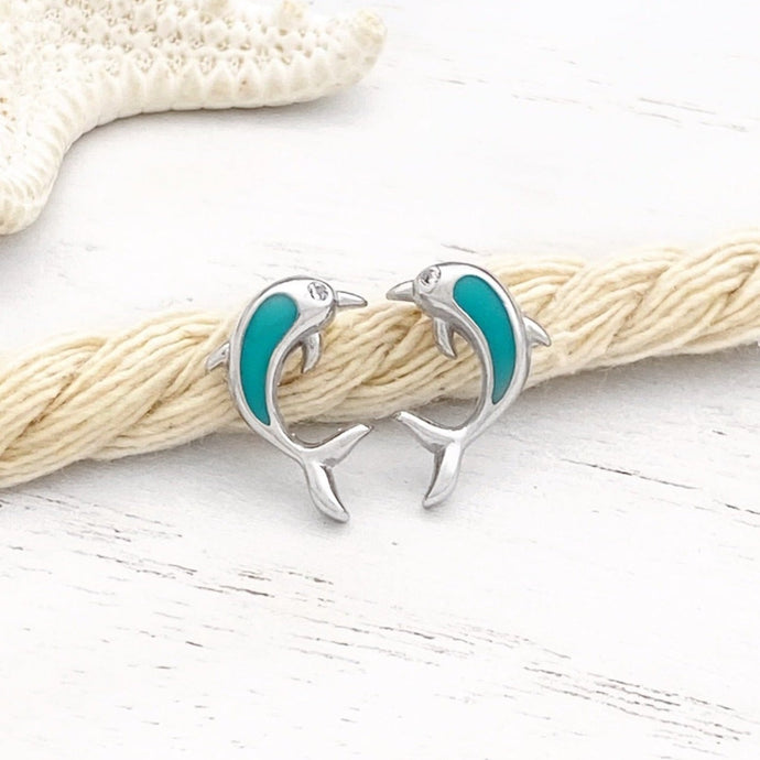Dolphin Stud Earrings are placed on a thick rope while being displayed on a white wooden surface.