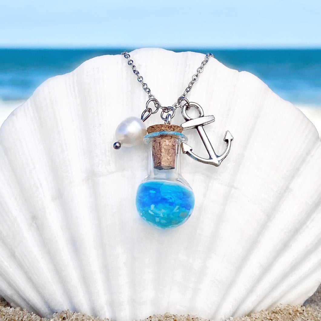 Drift Bottle Anchor Necklace is hung on a big white oyster shell on the beach.