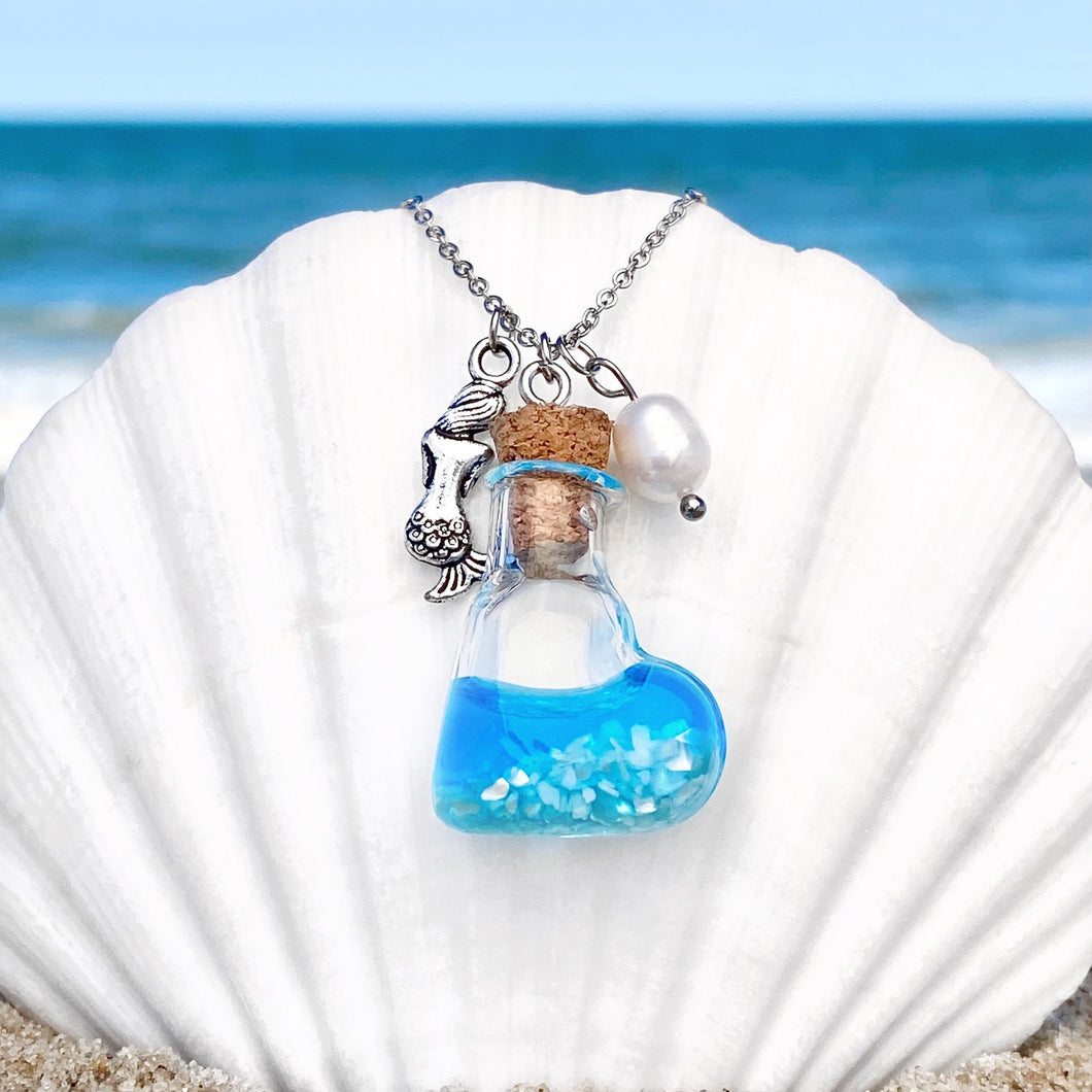 Drift Bottle Mermaid Necklace is hung on a big white oyster shell on the beach.