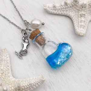 Drift Bottle Mermaid Necklace displayed on a white wooden surface.