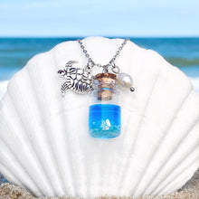 Load image into Gallery viewer, Drift Bottle Sea Turtle Necklace is hung on a big white oyster shell on the beach.