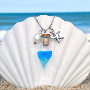 Drift Bottle Starfish Necklace is hung on a big white oyster shell on the beach.