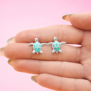 Enamel Sea Turtle Studs showcased between fingers for a close-up view.