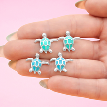 Load image into Gallery viewer, Enamel Sea Turtle Studs showcased between fingers for a close-up view.