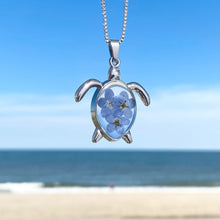 Load image into Gallery viewer, Forget Me Not Sea Turtle Necklace hanging against a blurred beach background, perfect for beach-themed accessories.