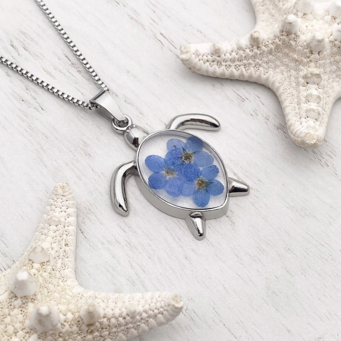 Forget Me Not Sea Turtle Necklace displayed on a white wooden surface, ideal spring jewelry.