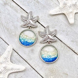 Glittering Ocean Starfish Earrings displayed on a white wooden surface.