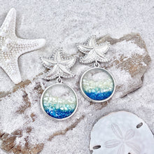 Load image into Gallery viewer, Glittering Ocean Starfish Earrings are displayed by being placed on top of a sand covered driftwood.