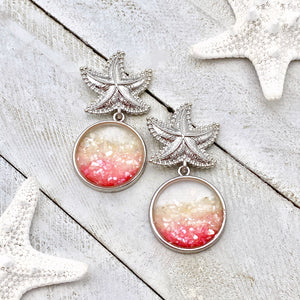 Glittering Ocean Starfish Earrings are displayed on a white wooden surface.