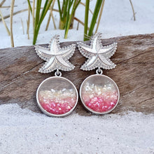 Load image into Gallery viewer, Glittering Ocean Starfish Earrings are displayed by being placed on top of a driftwood on the sand.