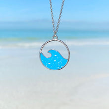 Load image into Gallery viewer, Glittering Wave Necklace is hanging up close with a beach background blurred.