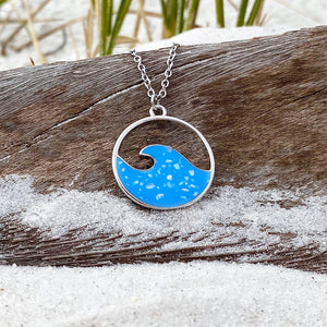 Glittering Wave Necklace is displayed by being placed on top of a driftwood on the sand.