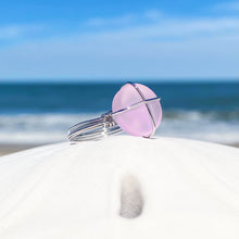Load image into Gallery viewer, Hand-Wired Pink Sea Glass Ring is sitting on top of a white dome against a blurred beach background.