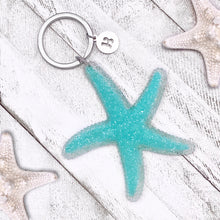 Load image into Gallery viewer, Happy Starfish Keychain displayed on a white wooden surface.
