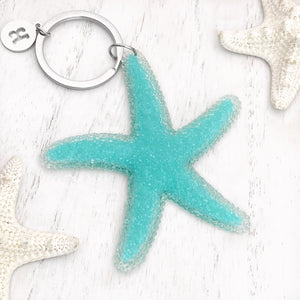 Happy Starfish Keychain displayed on a white wooden surface.