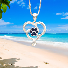 Load image into Gallery viewer, Heart Paw Necklace hanging close for a shot with a beach background.