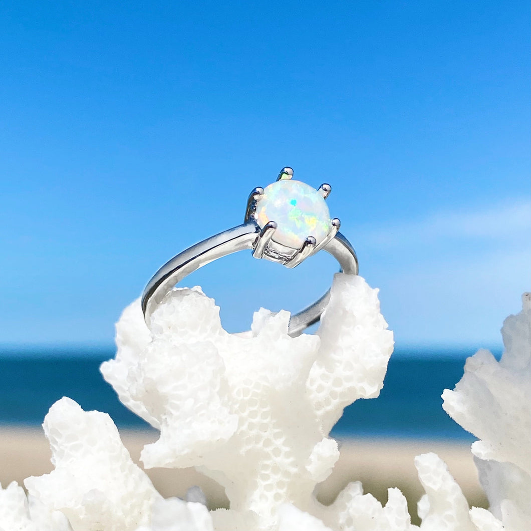 Minimalist Opal Ring displayed by being placed on top of white artificial coral with a blurred beach background.