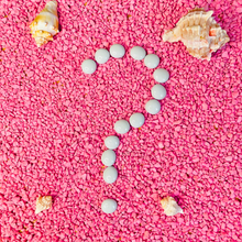 Load image into Gallery viewer, Several white smooth rocks forming a question mark on top of pink pebbles covering the ground.