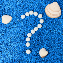 Load image into Gallery viewer, Several white smooth rocks forming a question mark on top of blue pebbles covering the ground.