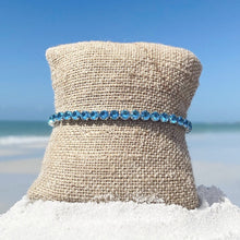 Load image into Gallery viewer, Ocean Blue Zircon Tennis Bracelet displayed by being wrapped around a canvas cloth placed on the sand.
