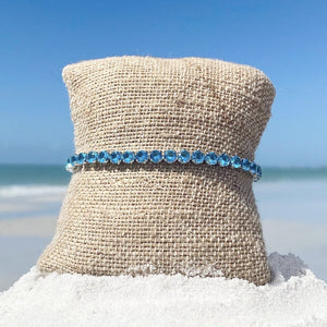 Ocean Blue Zircon Tennis Bracelet displayed by being wrapped around a canvas cloth placed on the sand.